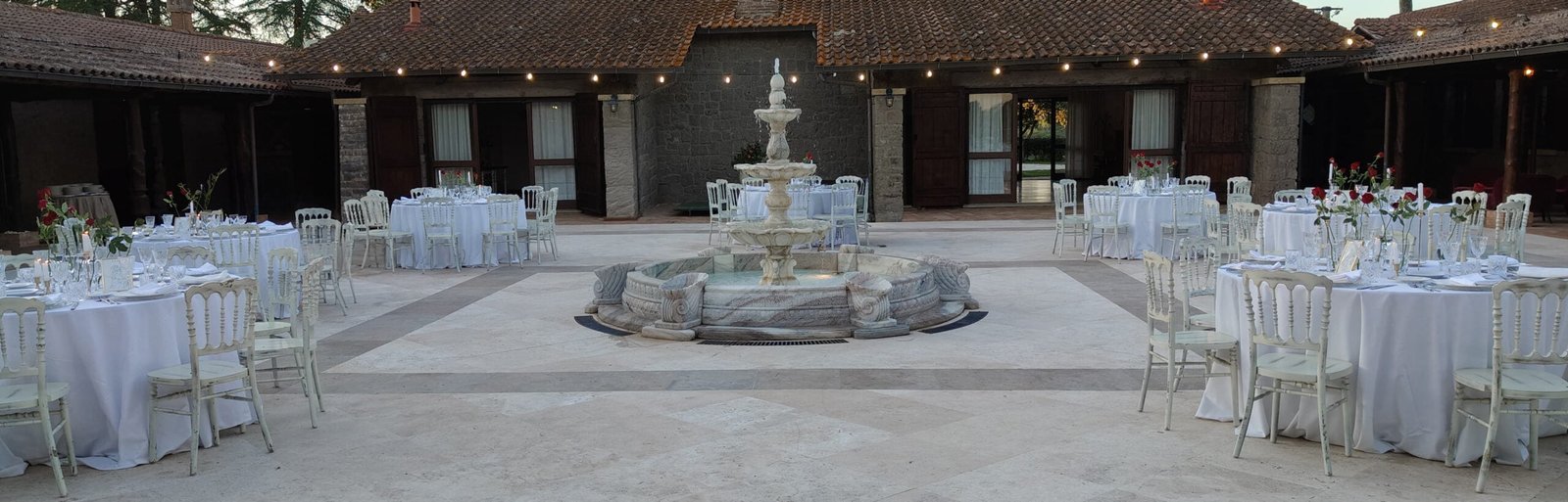 Evento Elegante alla Tenuta Domina Flaminia Area evento della Tenuta Domina Flaminia allestita con tavoli da ricevimento e una fontana centrale, pronta per una celebrazione speciale.